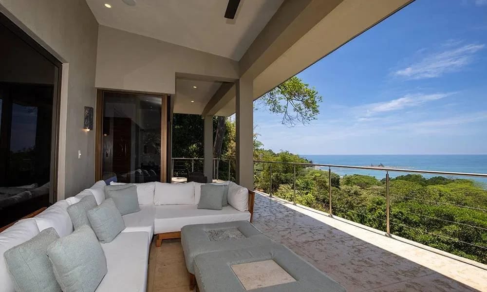 Casa Ola Vista · 7. A covered outdoor living area with an L-shaped sofa opens to panoramic views of the Pacific Ocean and verdant jungle canopy.