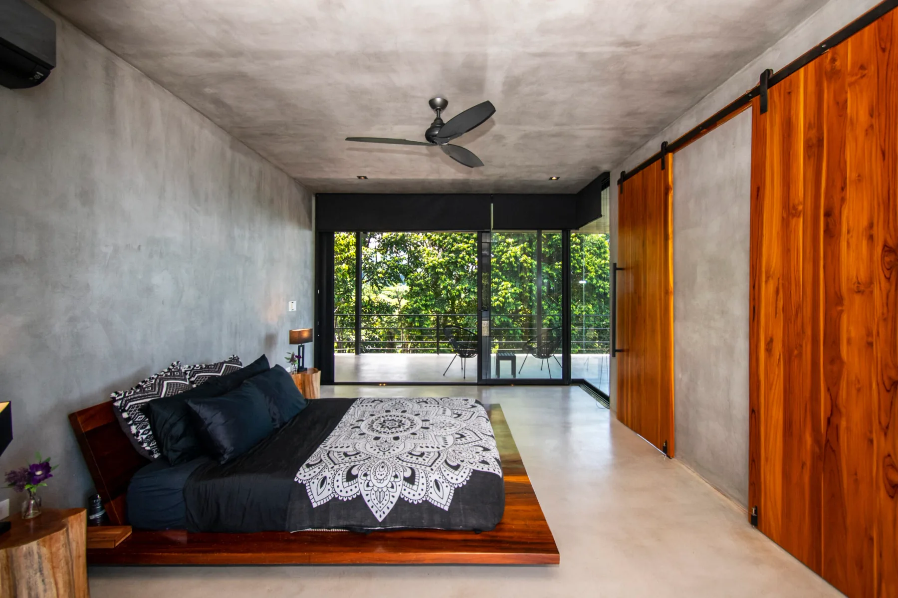 A bedroom with a bed, wood-paneled doors, and glass doors opening onto greenery.