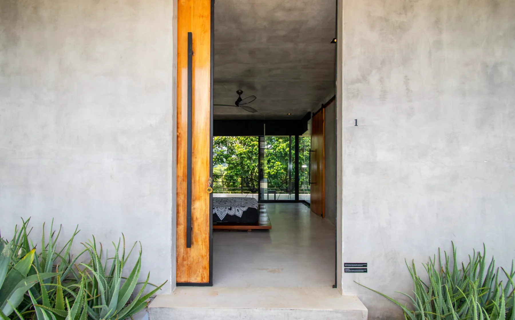 An open doorway leads into a bedroom with a bed and glass doors overlooking greenery.