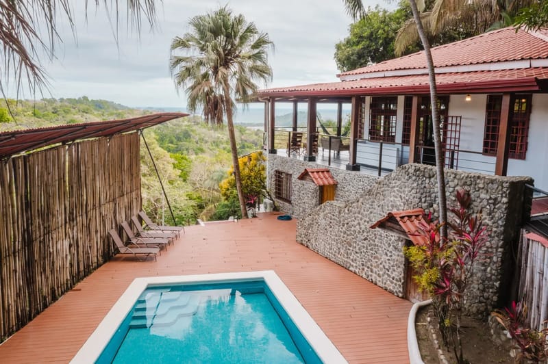 Casa Blue Wind · 22. A private tiled pool with steps is surrounded by a spacious wooden deck, leading to an elevated covered terrace offering tropical jungle and ocean views.
