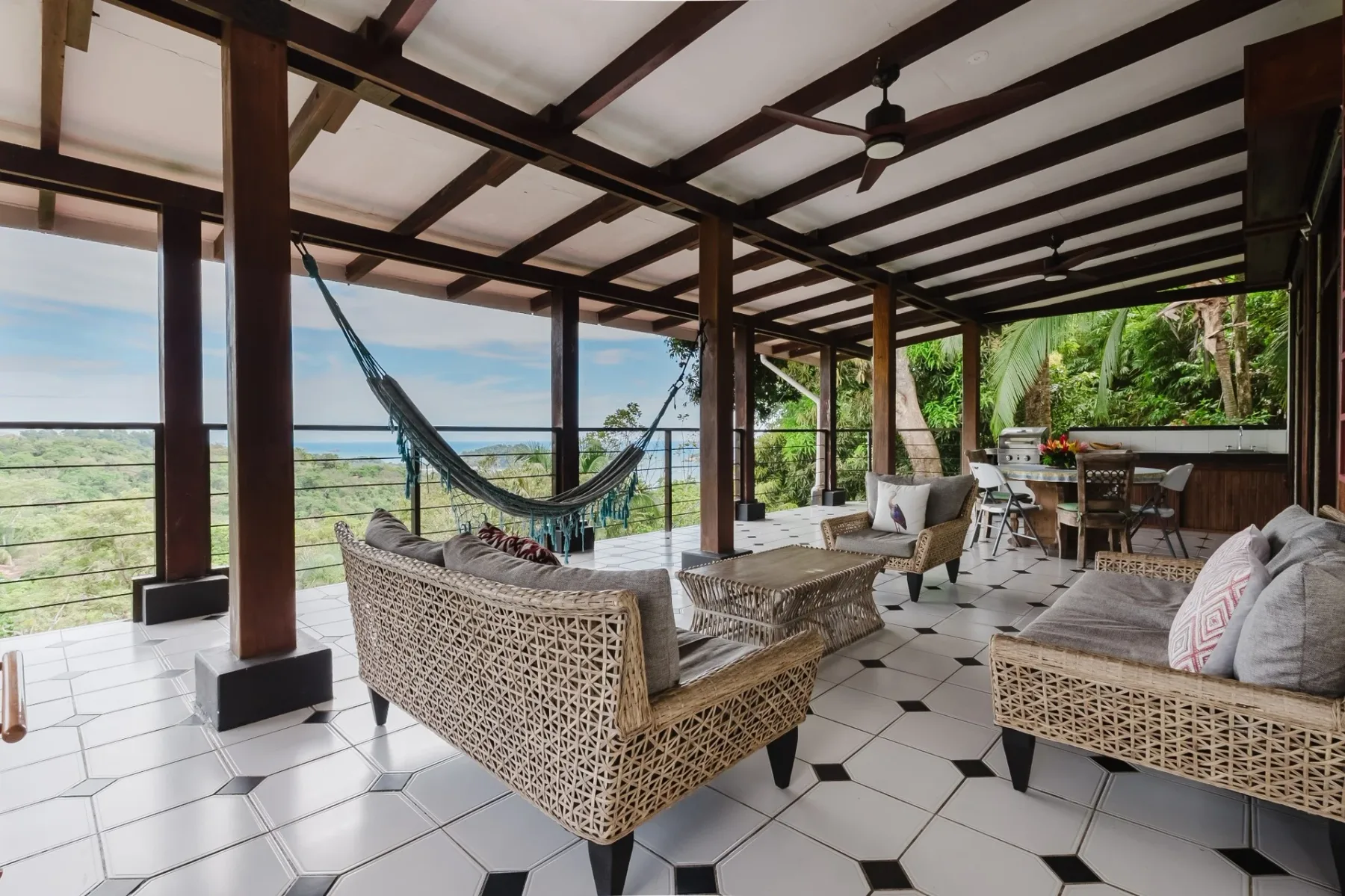 Casa Blue Wind · 7. This open-air terrace features a beamed ceiling, tiled floor, various seating arrangements, a hammock, and an outdoor kitchen, all overlooking panoramic jungle and ocean views.