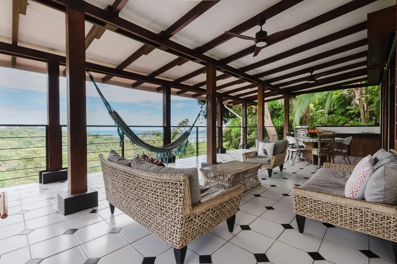 Casa Blue Wind · 7. This open-air terrace features a beamed ceiling, tiled floor, various seating arrangements, a hammock, and an outdoor kitchen, all overlooking panoramic jungle and ocean views.