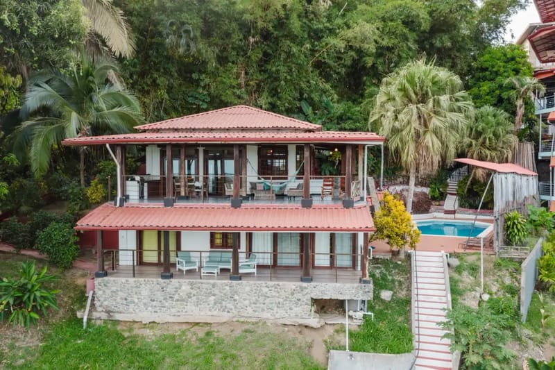 Casa Blue Wind · 30. A two-story villa with red tile roofs features open-air terraces on both levels and a private pool, surrounded by dense tropical greenery.