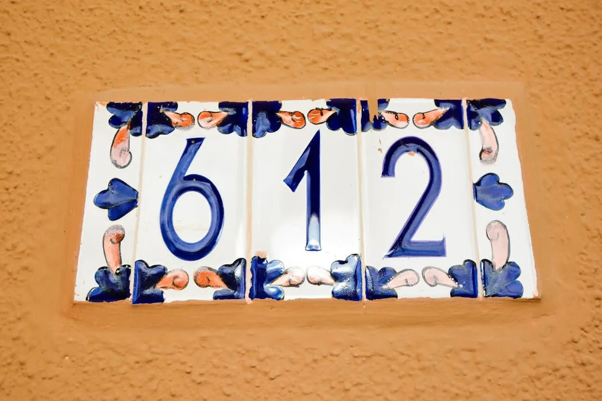 A decorative ceramic address plaque with blue numerals is mounted on a textured wall.