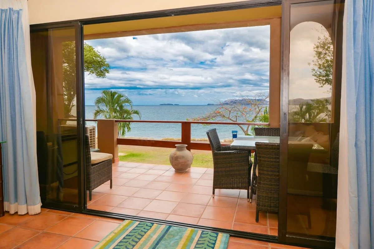An open patio overlooks the ocean, with outdoor seating and a potted plant.