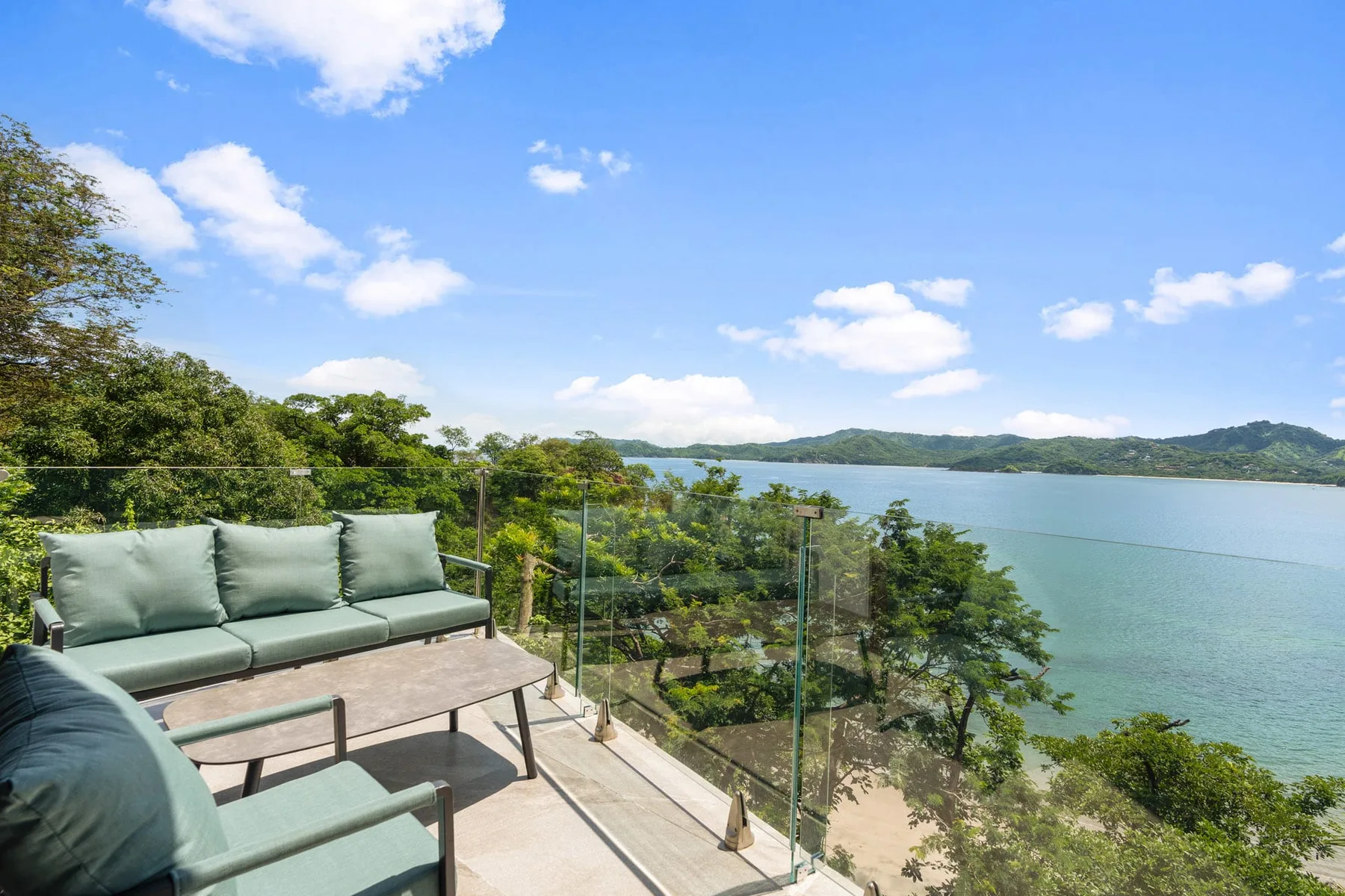 An outdoor terrace with seating overlooks a tree-lined bay.