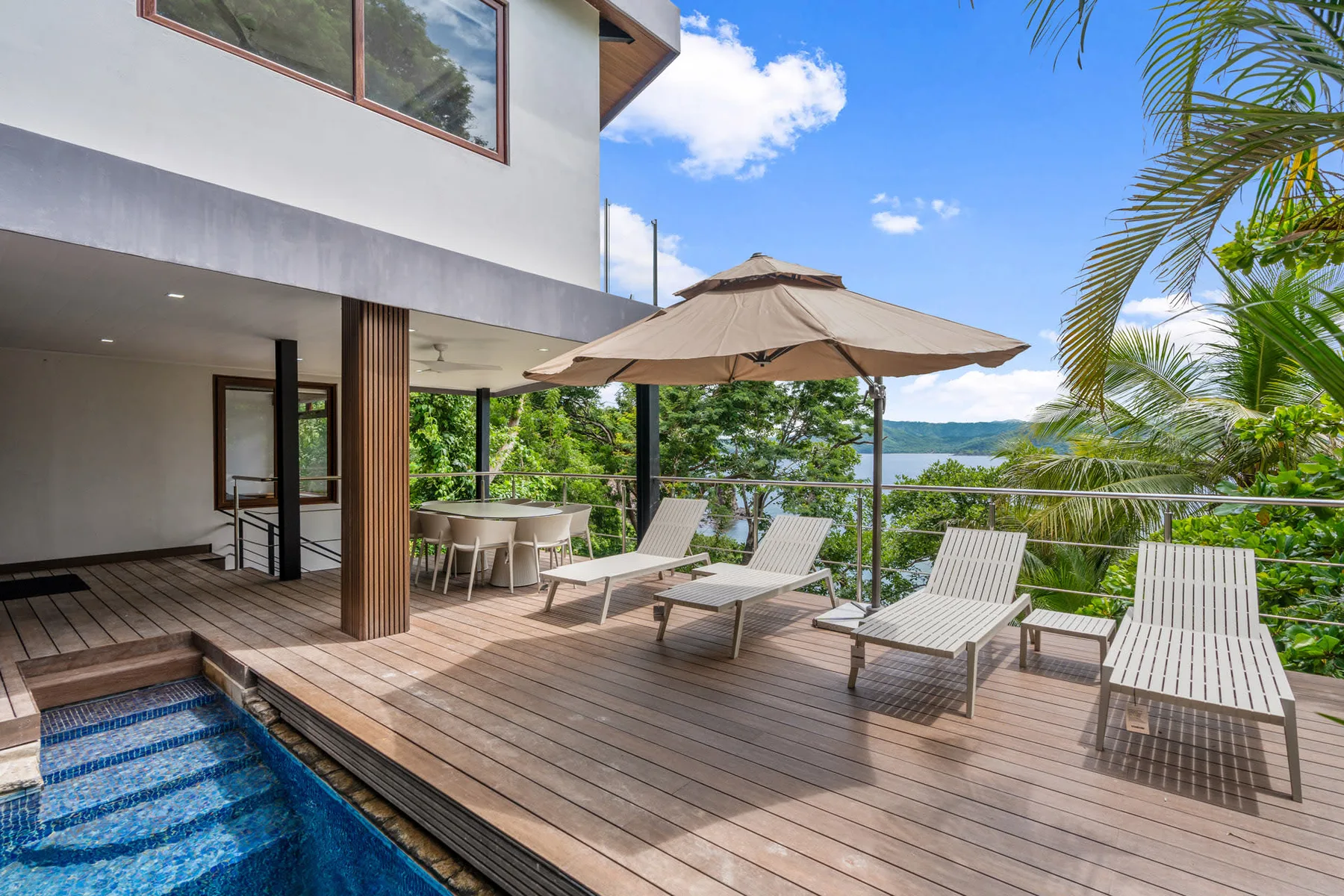 A wooden deck with lounge seating and an umbrella overlooks the water.