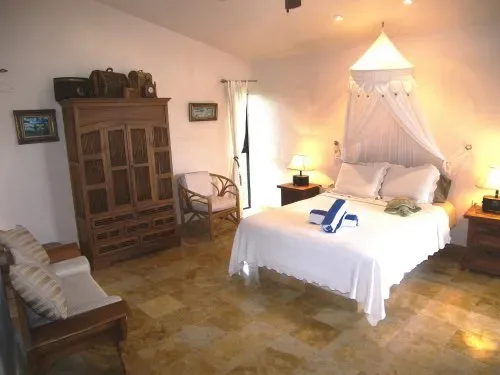 A bedroom with a canopied bed, wooden wardrobe, and tiled floor.