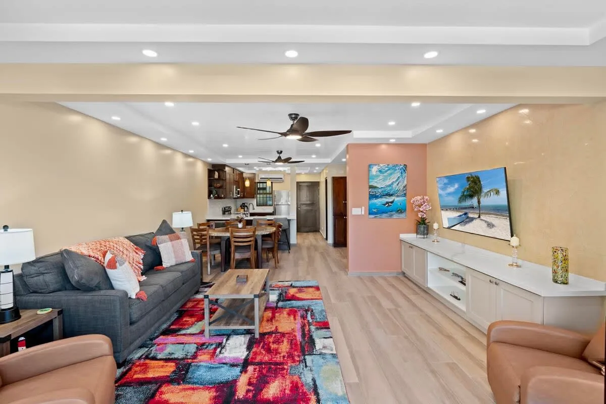 A living room with seating, a colorful rug, and an open kitchen in the background.