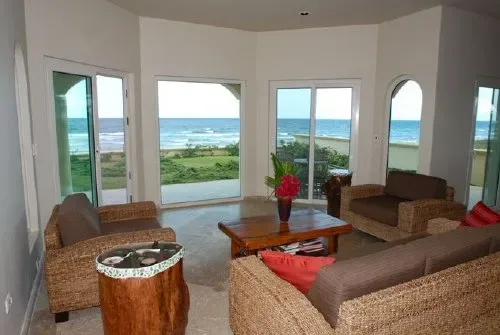 Una sala luminosa con asientos de mimbre y amplias ventanas con vista al mar.