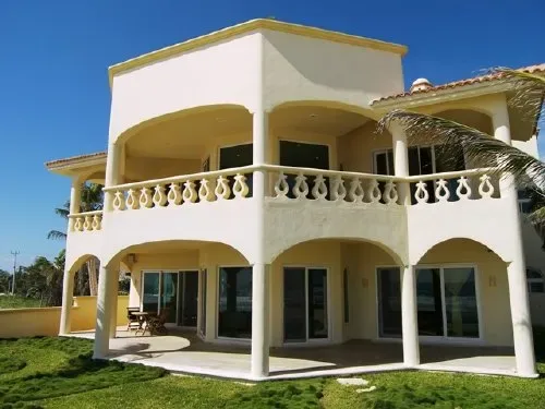 Una casa de dos pisos con balcones arqueados y césped verde bajo un cielo despejado.