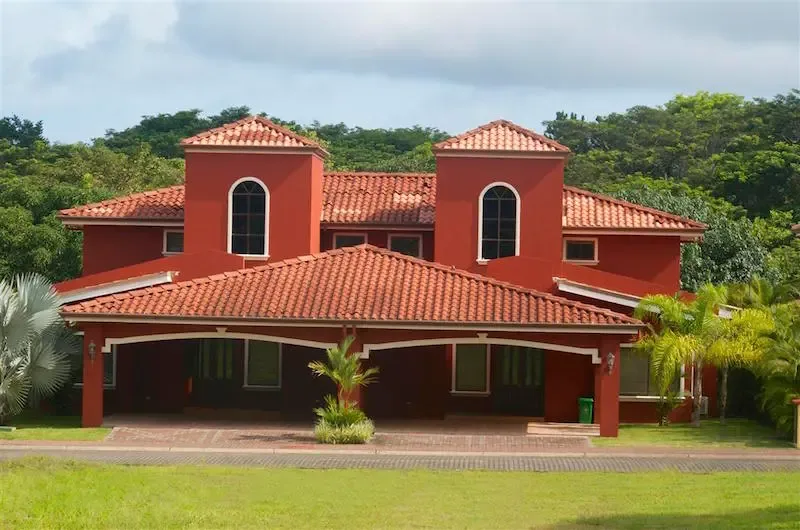 A red building with tiled roofs stands among greenery beneath a cloudy sky.