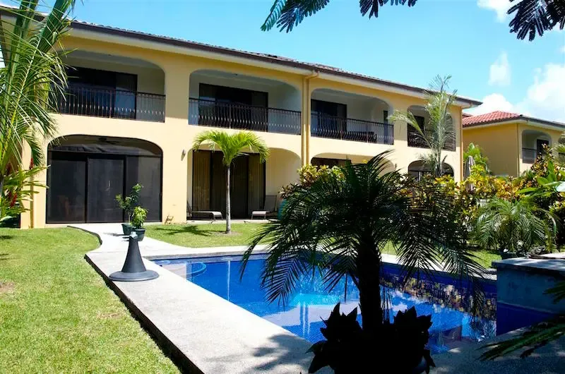 A sunny courtyard with a blue swimming pool beside a two-story building.