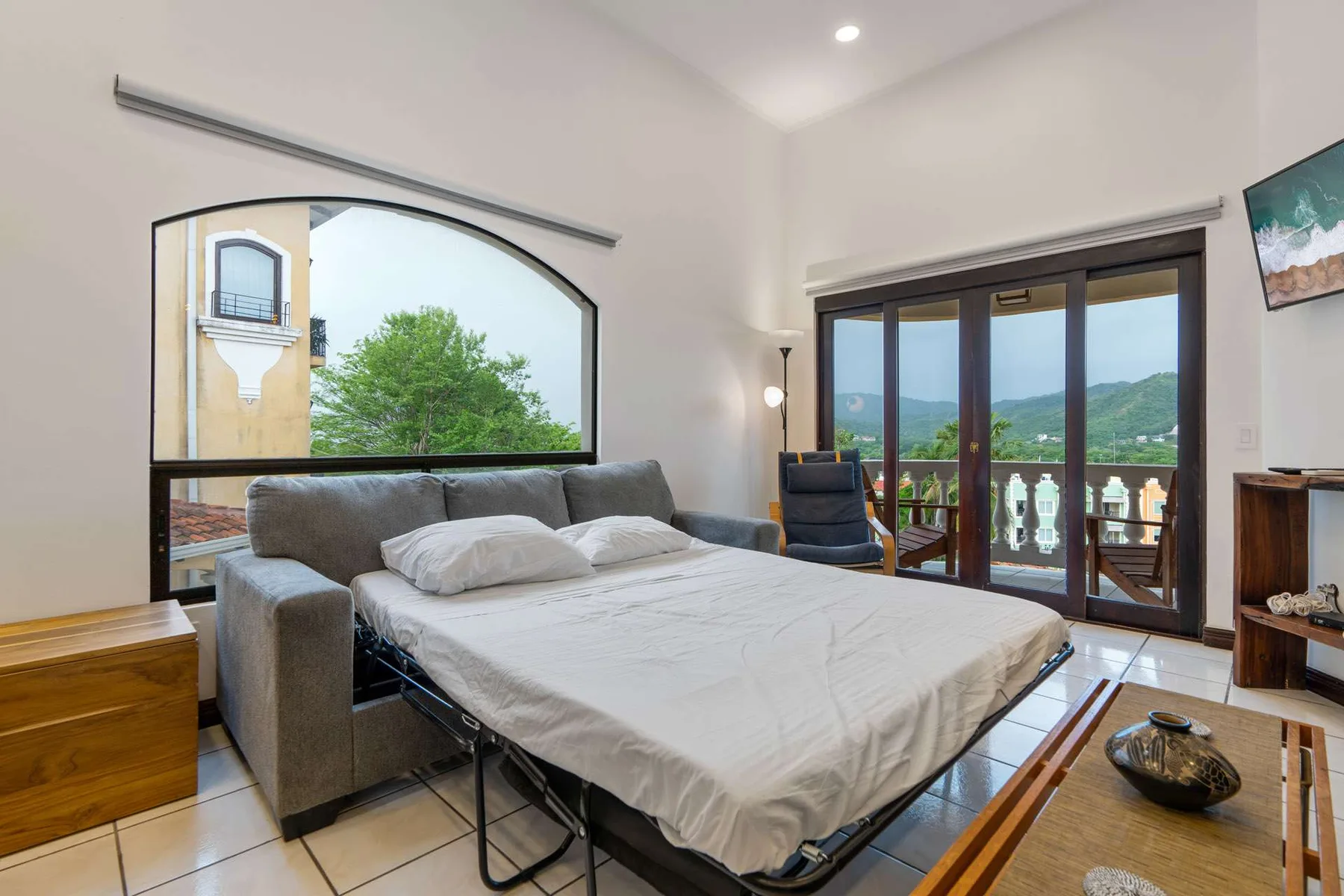 A bedroom with a bed in front of large windows overlooking a green landscape.