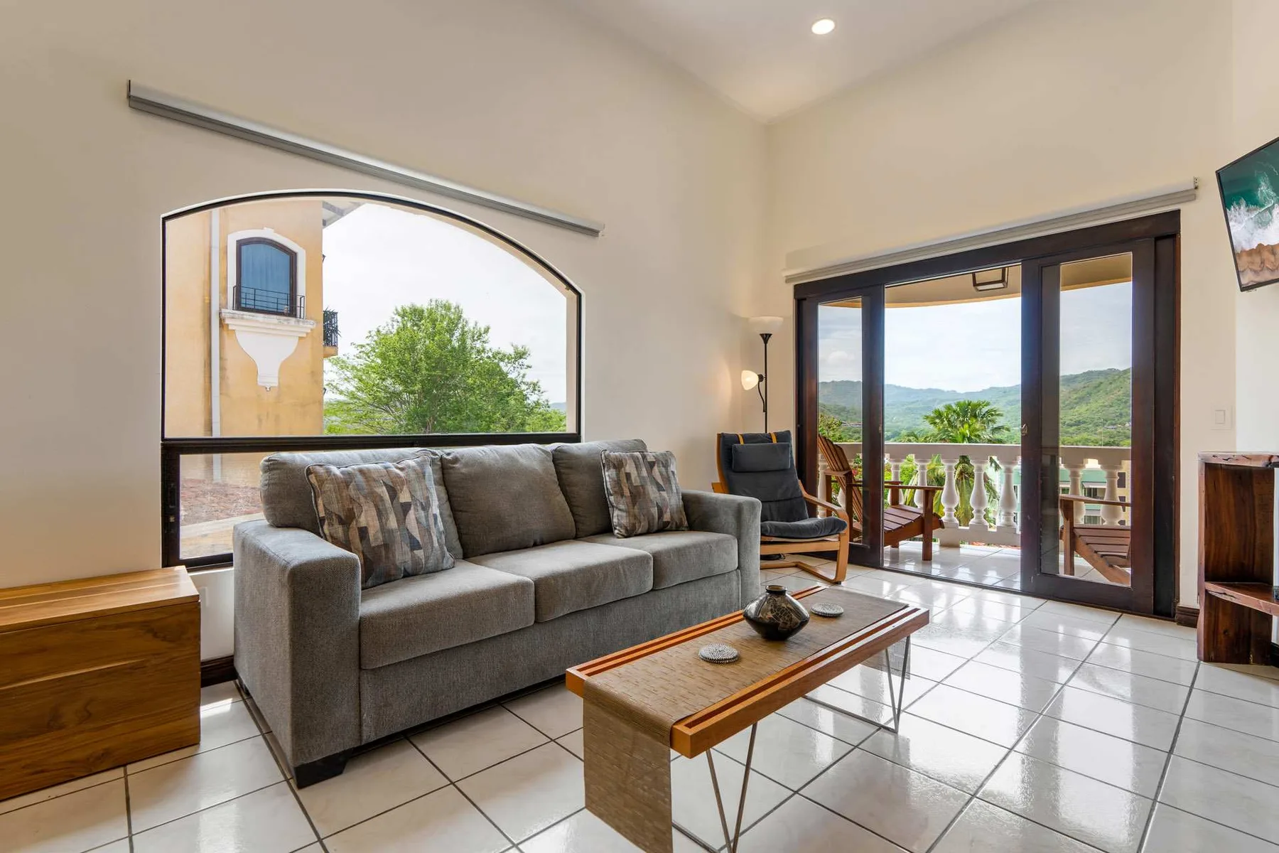 A living room with a gray sofa and glass doors opening onto a balcony.