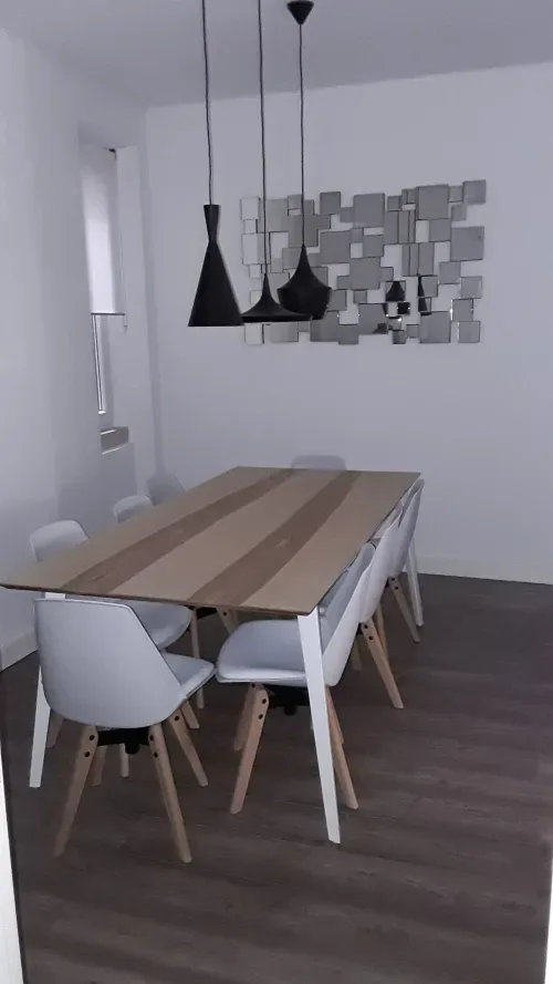 Un comedor con una mesa larga, sillas y lámparas colgantes.