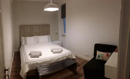 Un dormitorio con una cama bien hecha, una mesita de noche y un asiento negro.