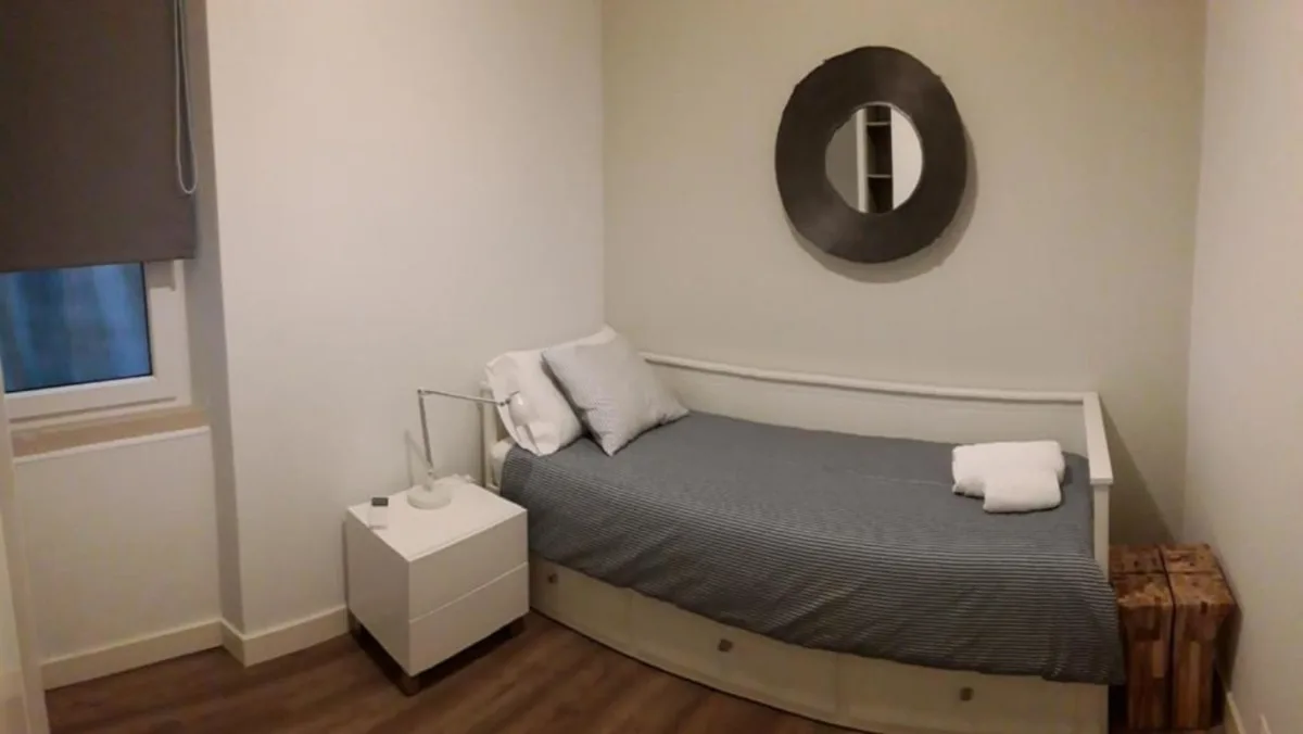 Un dormitorio con una cama individual, una mesita de noche y un espejo redondo en la pared.