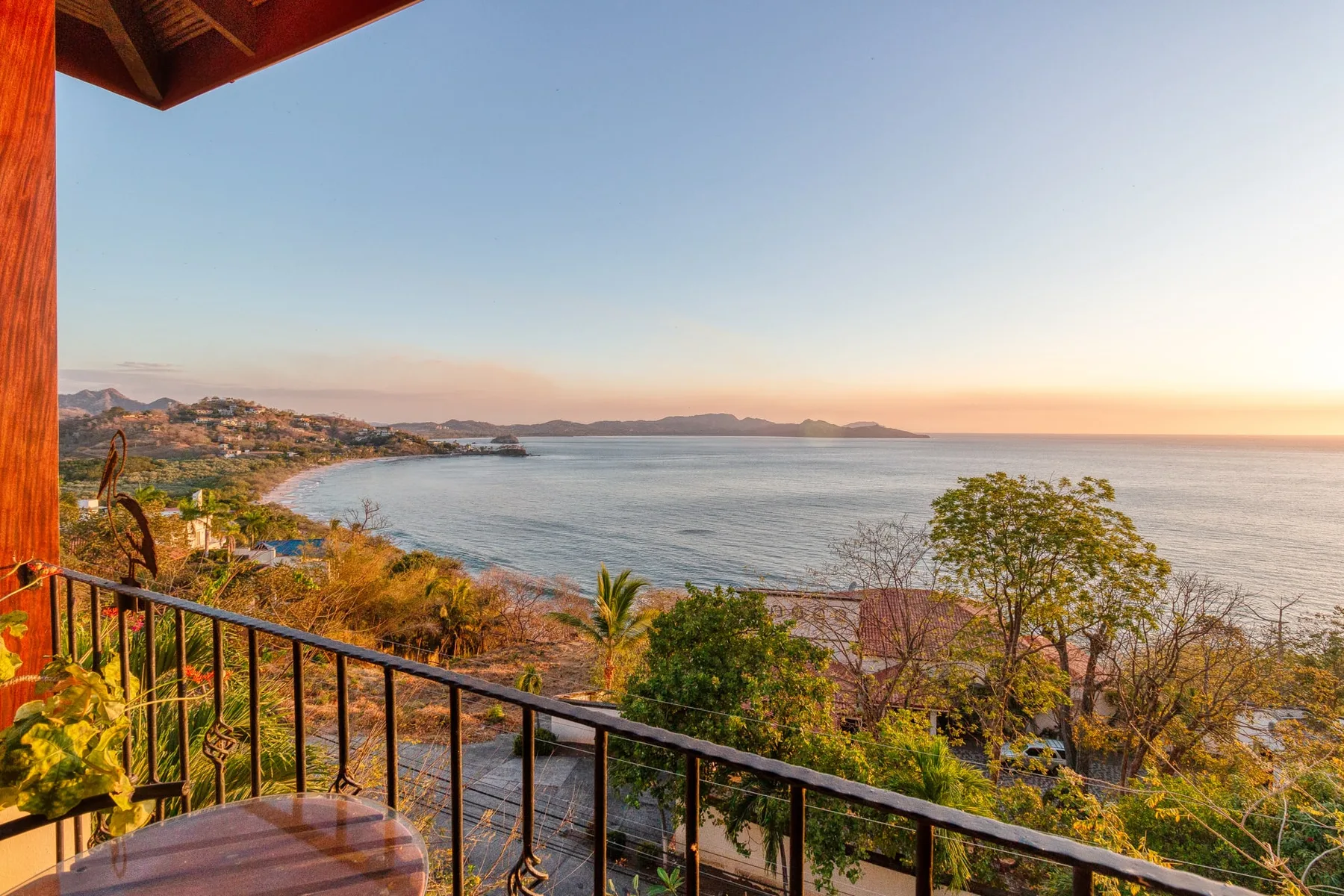 A balcony overlooks a calm bay and a distant coastline at sunset.