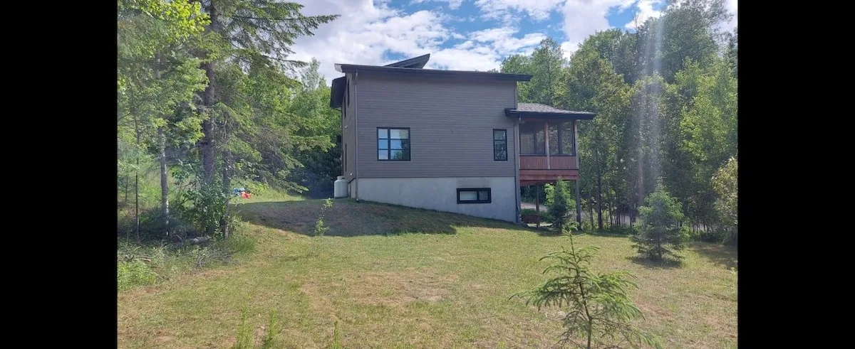 Una casa moderna se alza en un claro cubierto de hierba y rodeado de árboles.