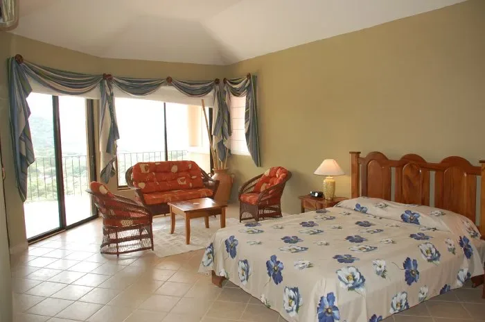 Un dormitorio con una colcha floral y una zona de estar junto a grandes ventanas.