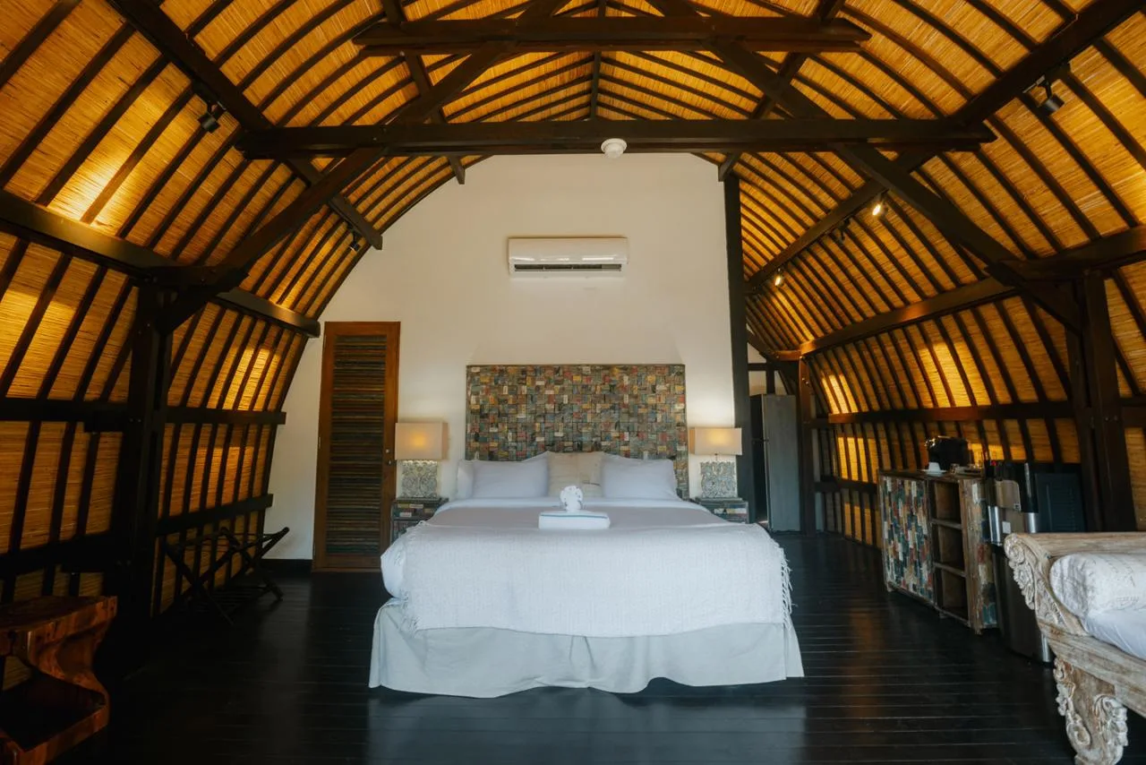 Un dormitorio con una cama blanca bajo un alto techo arqueado de vigas de madera a la vista.