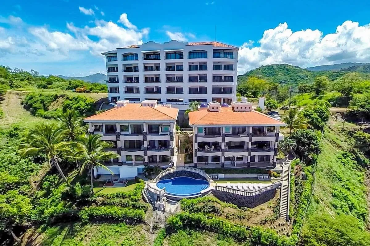 A multi-story resort building overlooks two smaller buildings and a curved swimming pool.