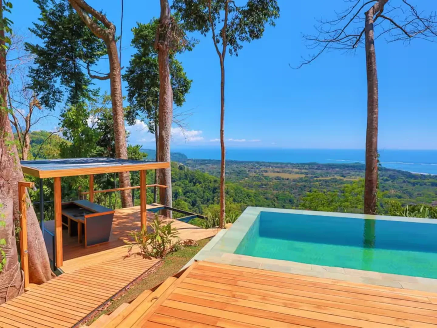 Una piscina al aire libre y una terraza de madera dan a un paisaje verde y al mar.