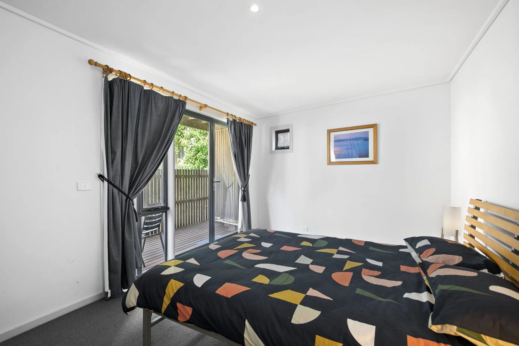 Un dormitorio con una colcha estampada junto a una puerta acristalada con cortinas.