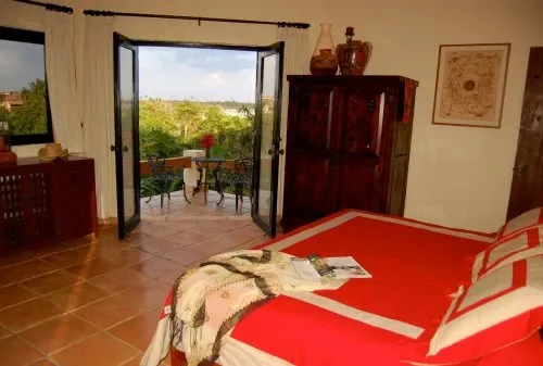 Un dormitorio con una cama roja y puertas abiertas hacia un balcón.