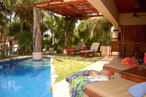 Una piscina tropical al aire libre junto a un patio sombreado con asientos.