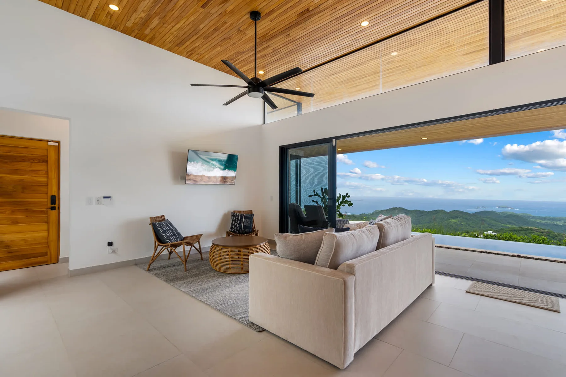 A bright living room opens onto a wide view of green hills and sky.