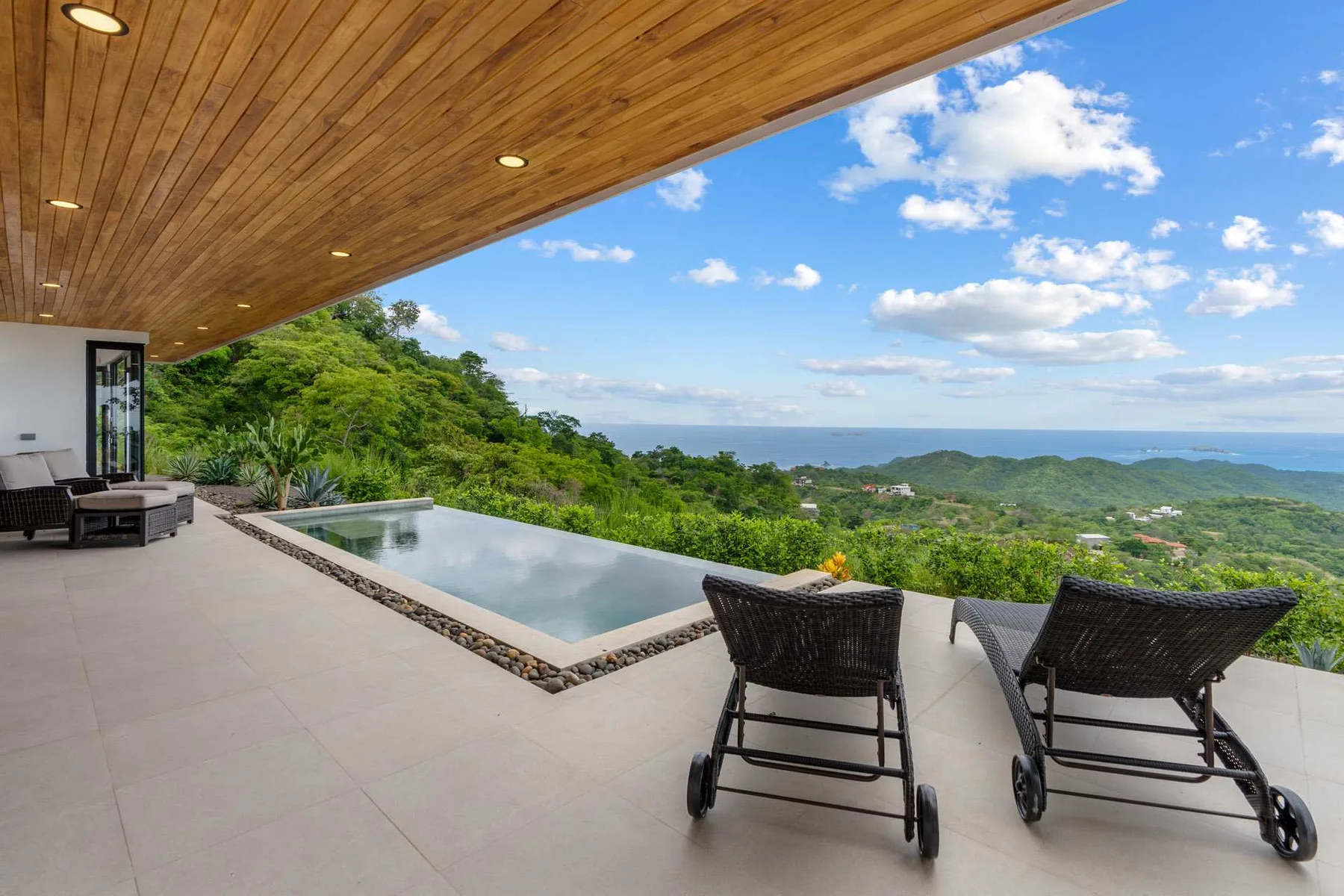 A terrace with a swimming pool and lounge seating overlooks green hills.