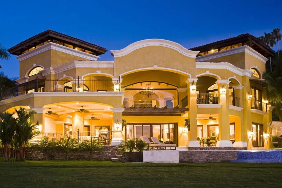 A large illuminated building with arched balconies stands against the evening sky.