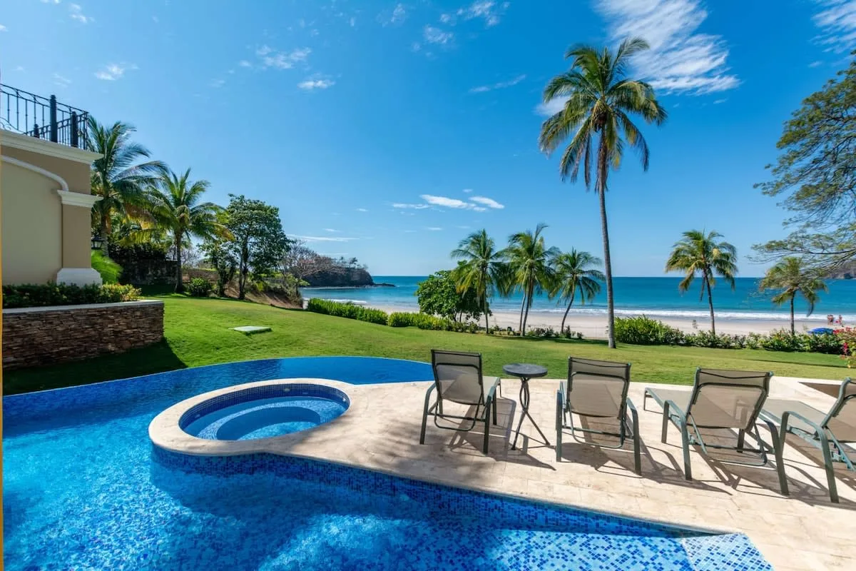 A poolside patio overlooks a grassy lawn and the ocean.