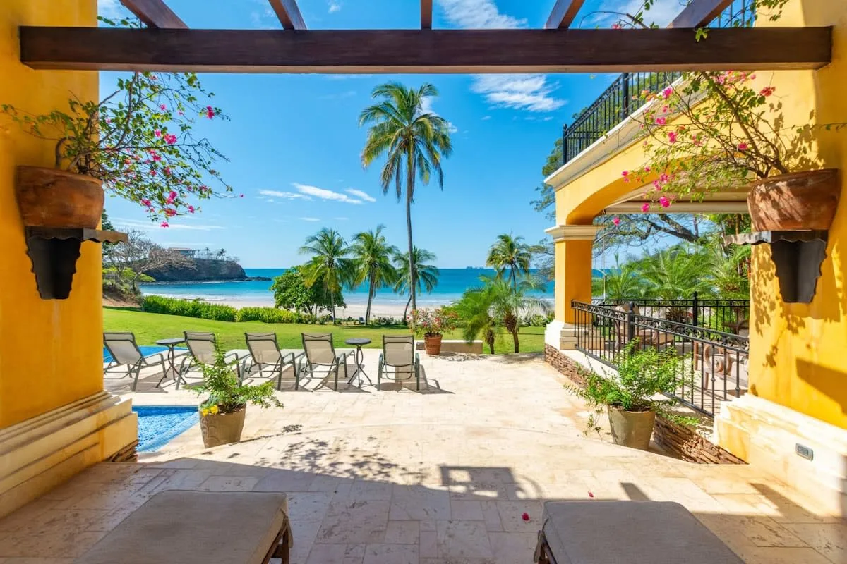 A seaside patio with outdoor seating overlooks a lawn and the ocean.