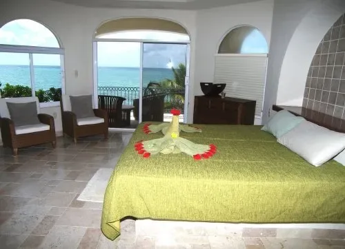 Un dormitorio con una cama cubierta de verde y ventanas arqueadas con vista al agua.