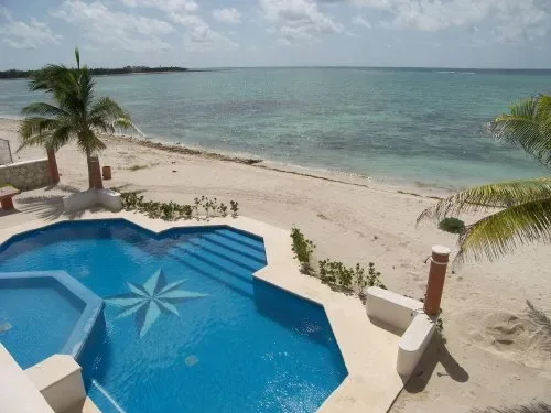 Una piscina azul está junto a una playa de arena y el mar.