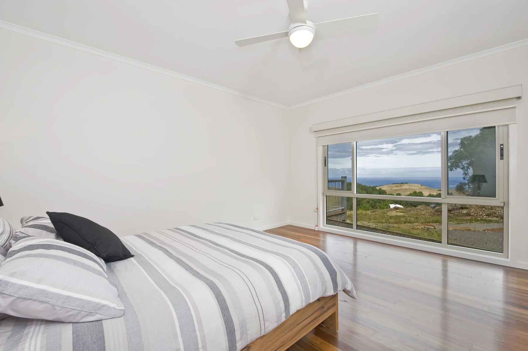 Un dormitorio con una colcha a rayas y una gran ventana con vistas a la costa.