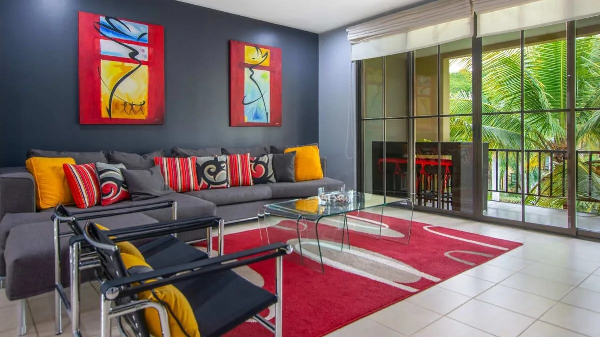 A living room with a gray seating area, colorful artwork, and a red rug.