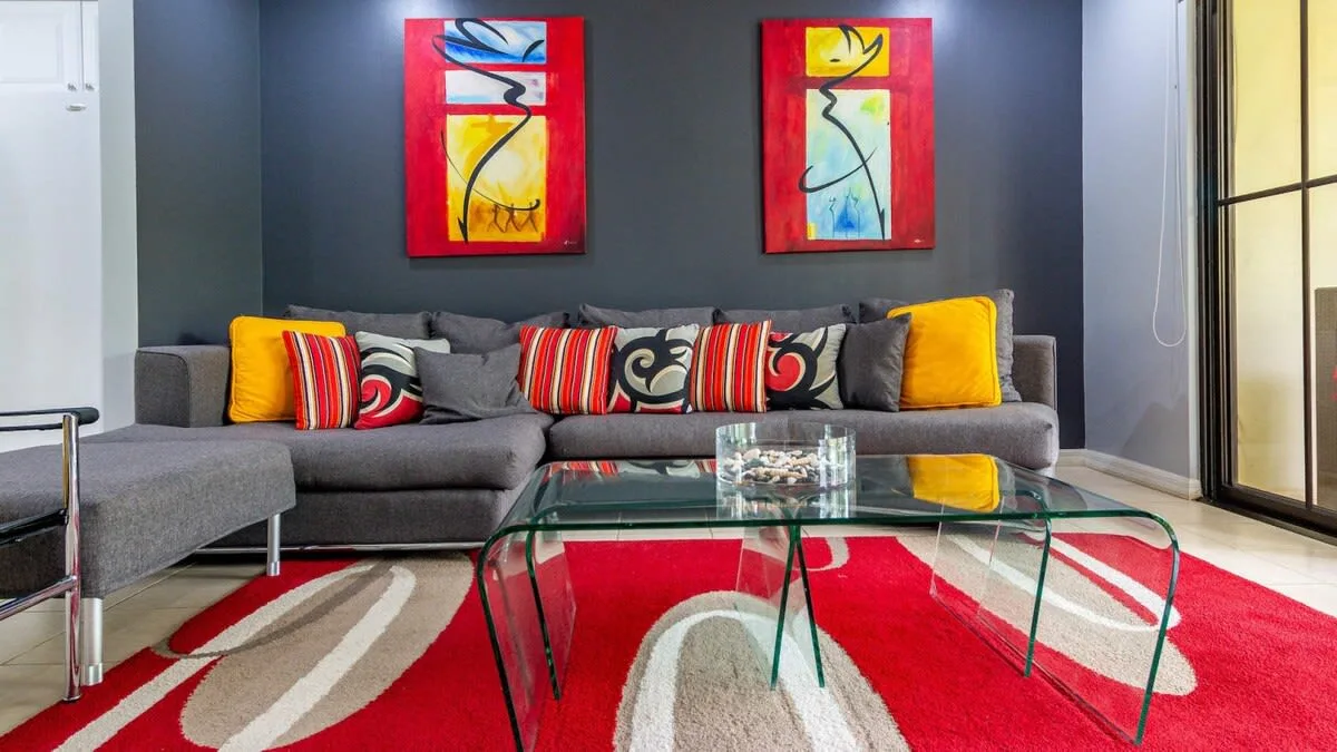 A living room with a gray sectional sofa, glass coffee table, and colorful wall art.