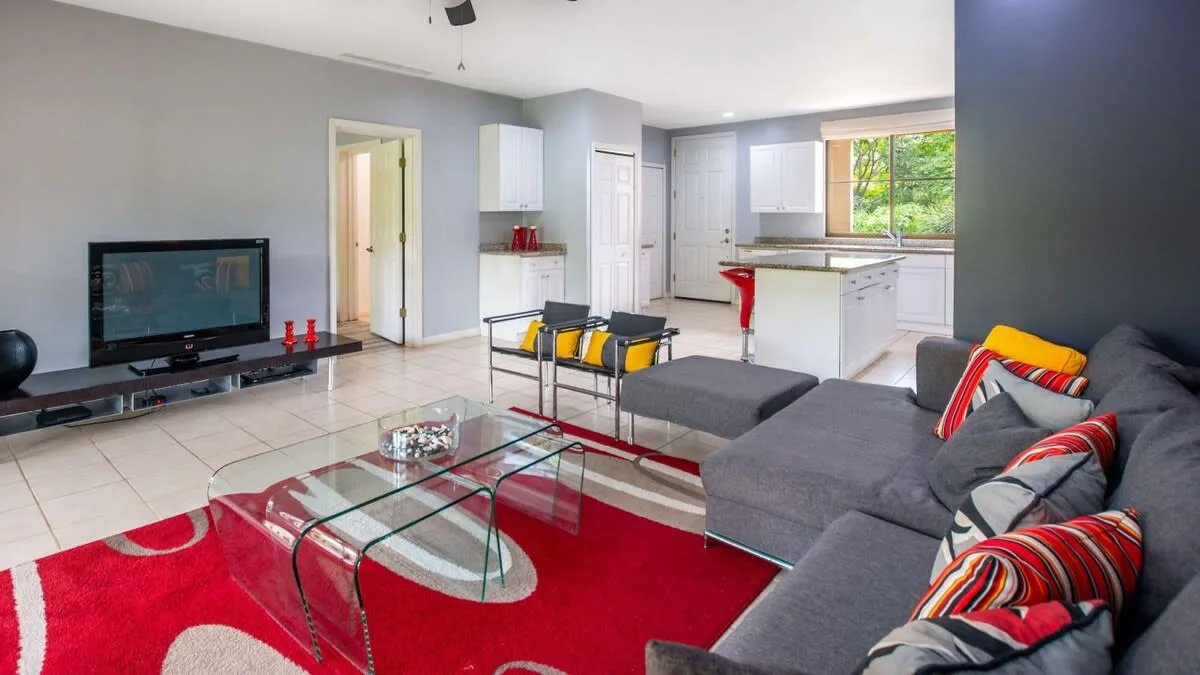 A bright open-plan living room and kitchen with a sectional seating area and glass coffee table.