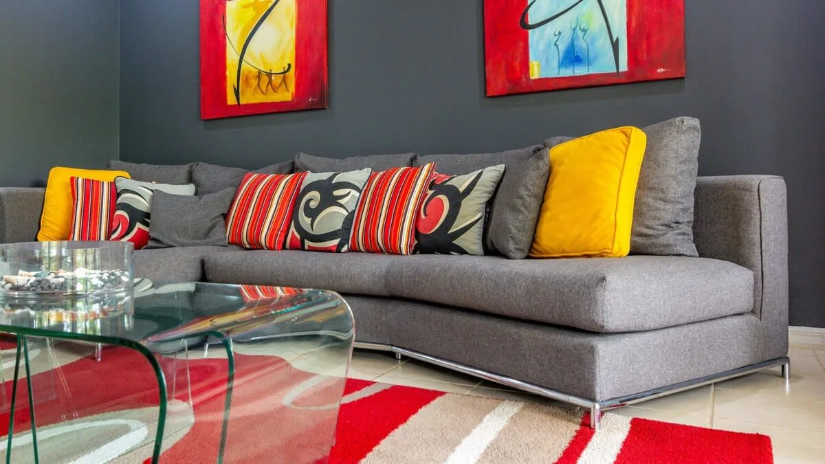 A living room with a gray sectional and colorful cushions beside a glass coffee table.