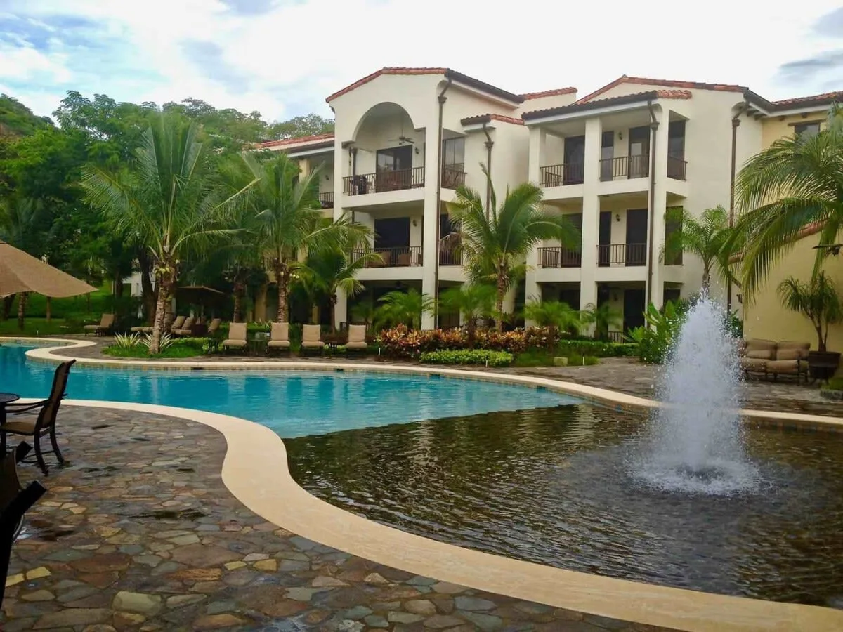 A swimming pool with a fountain sits in front of a multi-story building.
