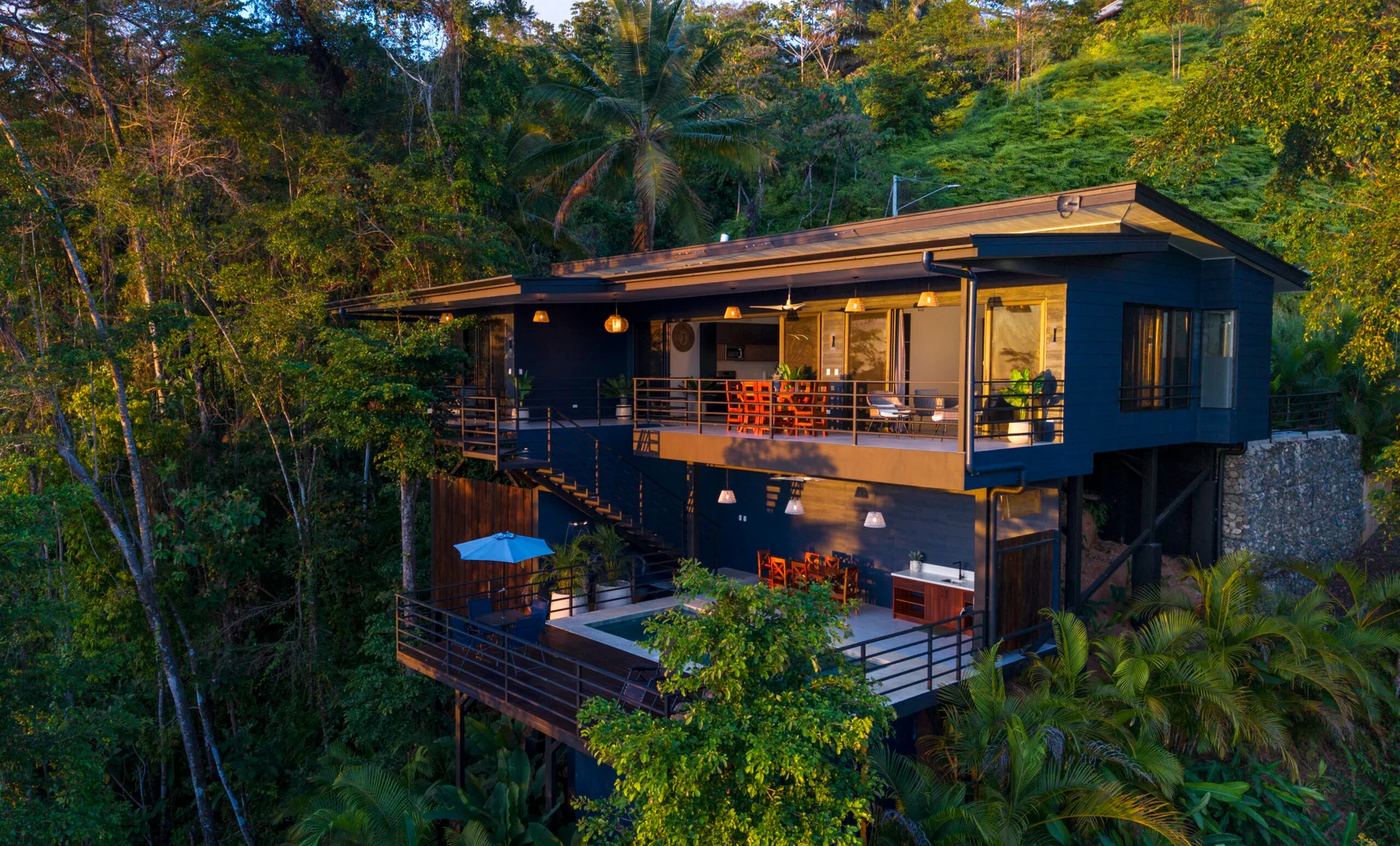 Una casa moderna con terrazas abiertas está rodeada de árboles frondosos.