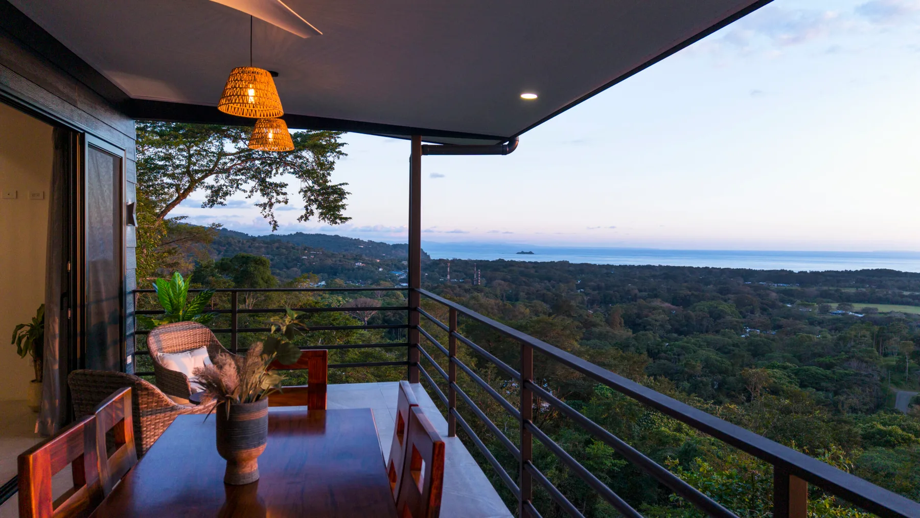 A covered balcony dining area overlooks green hills and the sea.