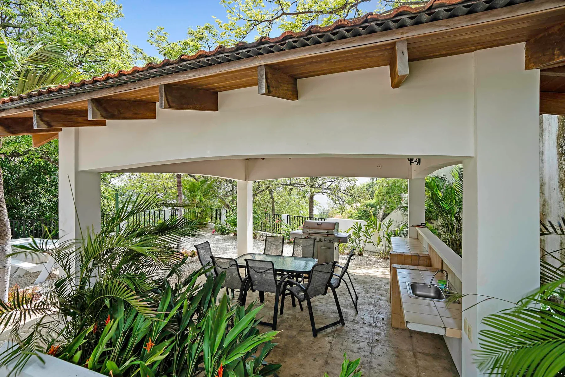 A covered outdoor dining area opens onto a leafy garden.