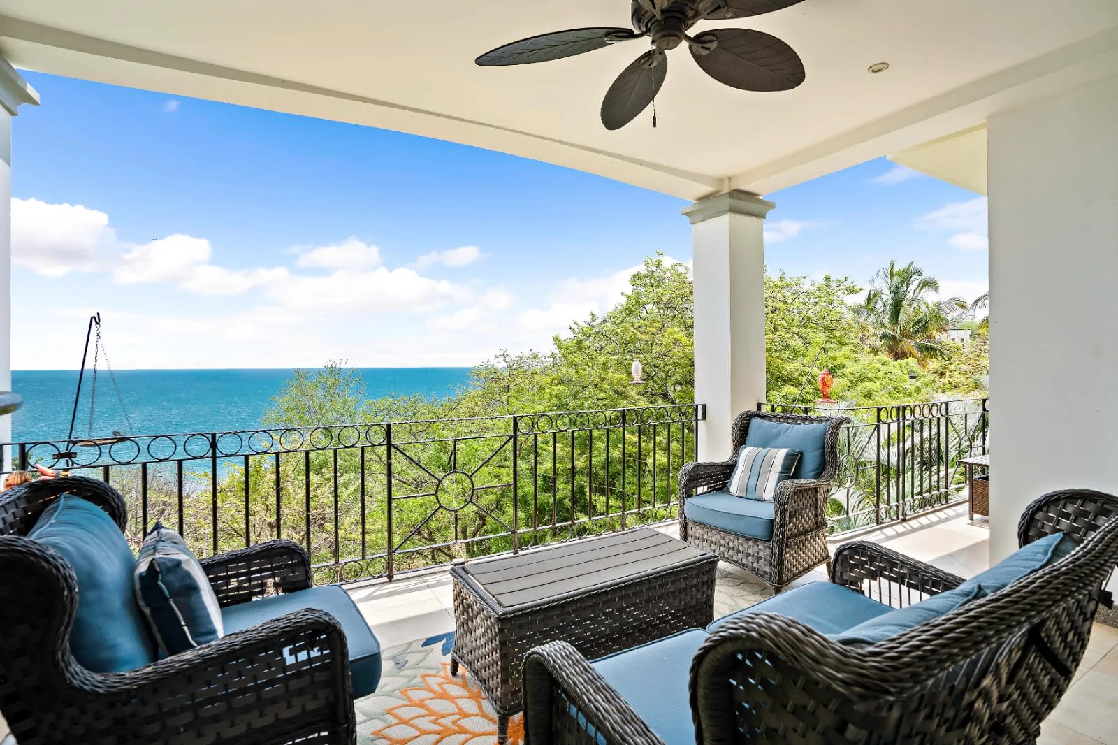 A covered outdoor seating area overlooks the ocean, with cushioned wicker furniture.
