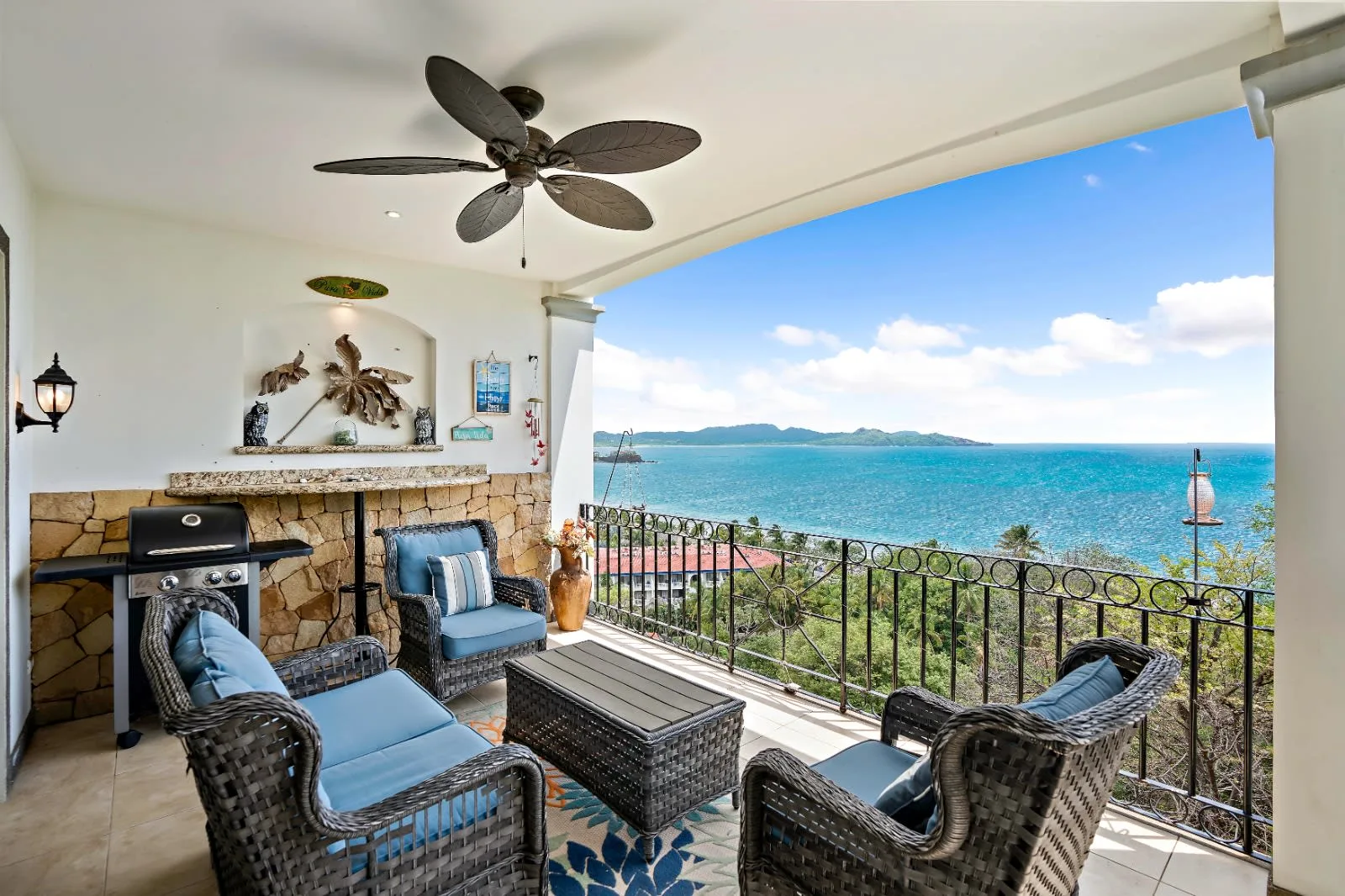 A covered patio overlooks the ocean, with woven seating and a stone fireplace.