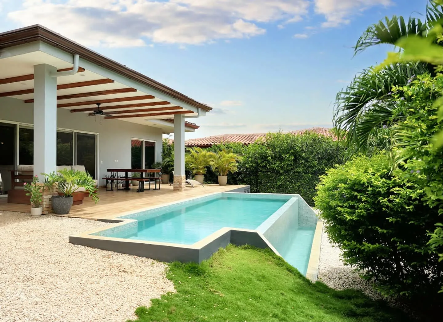 An outdoor swimming pool beside a covered patio and green garden.